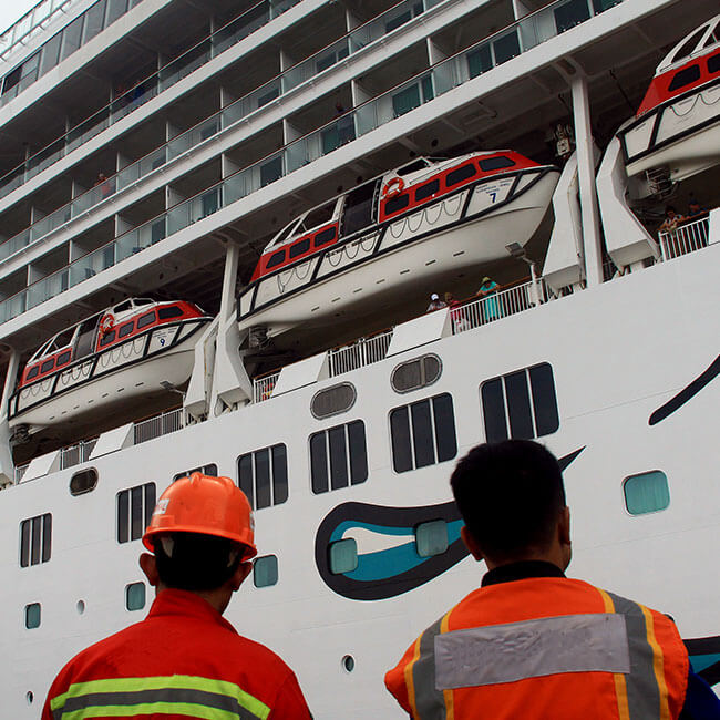 Two workers looking at the cruise lifeboats